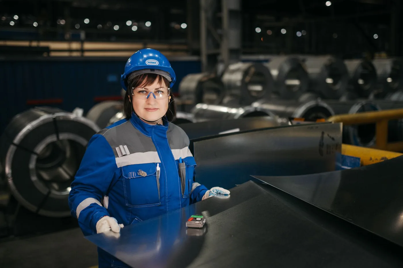 A worker in safety gear inspecting metal sheets in a factory